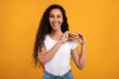 © Prostock-studio - A smiling woman with curly hair stands in front of a vibrant yellow background. She holds a big burger in her hands, excited about her tasty treat. This is a joyful moment celebrating indulgent food.