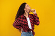 © Prostock-studio - A hungry woman is taking a big bite of a delicious burger in a studio. She is smiling and wearing a stylish outfit, set against a bright yellow background.