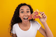 © Prostock-studio - Excited young woman smiles widely while holding a pepperoni pizza slice, showcasing her joy over a vibrant yellow-orange background. A true lover of junk food and tasty meals.