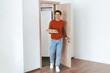 © Prostock-studio - A young man enters a bright, modern apartment holding a food delivery in takeout containers. He looks happy and relaxed, ready to enjoy his meal after a busy day.