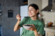 © Lumos sp - Portrait of a young woman preparing and eating breakfast, drinking juice in the kitchen at home