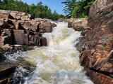 Rocky river rapids flowing through narrow gorge in summer. Fast and powerful river rapids flowing through a rocky canyon surrounded by lush green forest.