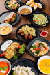 © bondvit - Overhead flat lay of assorted restaurant dishes, soups and salads on wooden table
