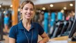 © mila103 - A friendly staff member stands at the front desk of a fitness center, welcoming visitors with a smile and offering assistance. The gym is bustling with people engaging in workouts.