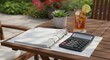 © photoplotnikov - Open binder with calculator on patio table near iced tea and succulent in garden setting