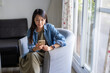 © leungchopan - Woman using smartphone while relaxing at home on sofa