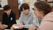 © CYBERPINK - Three young people sitting on the floor in a library or study area. they are all looking at a book and appear to be engaged in a conversation.