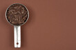 © nahhan - A stainless steel measuring cup filled with coarsely chopped dark chocolate is placed on a solid brown background with plenty of copy space