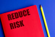 © Iryna - Red notebook with words reduce risk and yellow pencil on blue background