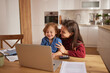 © Stockphotodirectors - A child and parent share a joyful moment at the dining table, looking at a laptop screen while surrounded by papers and a calculator. The warm environment highlights their connection.