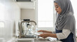© Nii_Anna - Muslim woman rinsing dishes in sink while standing in kitchen