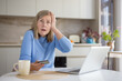 © Liubomir - Senior woman at home holding a credit card and laptop, experiencing stress and confusion while attempting online shopping or banking, reacting to a potential fraud or scam