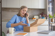 © Liubomir - Upset mature woman at home kitchen table complaining on smartphone about a received incorrect package after unboxing, expressing frustration and dissatisfaction
