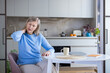 © Liubomir - Senior woman experiencing chronic neck pain and stiffness, touching her hurting neck and shoulder while sitting at a kitchen table, symbolizing health issues and physical discomfort in old age
