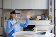 © Liubomir - Senior woman wearing a vr headset and interacting with virtual space, sitting at a kitchen table with a laptop, embracing modern technology and the metaverse