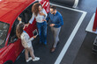 © Dragana Gordic - Friends and Family Discussing Car Purchase in Showroom Around Red SUV With Sales Representative Today