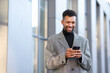 © New Africa - Smiling man in suit with smartphone on city street. Space for text