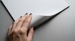 © MindRender - Hand turning a blank white paper page on a grey background, showcasing a clean and simple design for mockups and presentations
