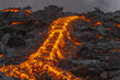 © Travel 'n' Lifestyle - View of fiery orange lava flows down a dark, rugged landscape, contrasting sharply against the cool, overcast sky, Reykjanes, Grindavíkurbaer, Iceland.