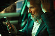 © Marko Geber - Mature businessman looking serious at smartphone in car at night