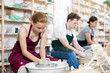 © JackF - Young woman teacher in apron shows students teenage girl and teenage boy how to sculpt ceramic product from raw clay on potter's wheel