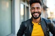 © Maryna - Hispanic man with beard smiles. He wears yellow shirt and black jacket outdoors. Person stands near building with glass windows. Man looks friendly and confident.