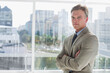 © wavebreak3 - Mature man standing arms crossed by glass window showing skyline, in suit and tie, copy space
