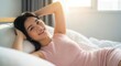 © Chalim - Serene morning bliss: A young Asian woman relishing cozy comfort in bed illuminated by soft sunlight