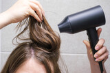 Young woman drying her hair with hairdryer in bathroom front view.