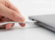 © Creativeraf - Hand plugging white charging cable into side of modern laptop