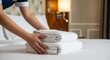 © Olga Ко - Gros plan d'une femme de chambre posant des serviettes propres sur un lit d'hôtel.