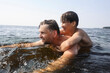 © Westend61 - Father and son smiling and playing together in the sea on summer day