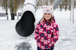 © Studio Peace - Little caucasian girl smiling in snow at playground, wearing bright pink jacket and bear hat.