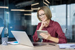 © Liubomir - Young businesswoman with glasses smiling, interacting with a digital tablet and laptop at her modern office desk, demonstrating productivity and technology integration