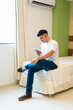 © Hugo - Happy man using phone while sitting on the corner of his bed.