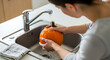 © Thiago - A woman meticulously washes a vibrant pumpkin under the running water of a kitchen faucet. The scene is illuminated, highlighting the freshness of the autumn harvest preparation.