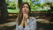 © Krakenimages.com - Woman clasps hands under chin and gazes anxiously to the side beneath sunlit green canopy in forest; concern.
