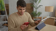© Krakenimages.com - Man holds tablet and uses touch controls in home space while young hispanic tenant organizes moving boxes using smartphone technology.