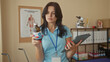 © Krakenimages.com - Young hispanic woman physiotherapist inspects medicine bottle and tablet in clinic treatment room; professional care focus trust.