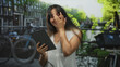 © Krakenimages.com - Woman holding tablet and hand covering face while smiling on a street by a canal in amsterdam outdoors; joy connection.