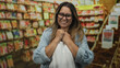 © Krakenimages.com - Woman with clasped hands at chest in a flower shop aisle surrounded by seed packets on shelves, smiling and wearing glasses; simple joy.