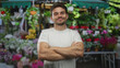 © Krakenimages.com - Man with crossed arms showing forearms at street flower stall surrounded by colorful potted flowers and hanging plants; local market confidence.