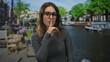 © Krakenimages.com - Woman wearing glasses and gray long sleeve top, finger to lips for silence on street by a canal in amsterdam; quiet secrecy.