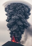 A large plume of black smoke rises from the top of a mountain