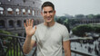 © Krakenimages.com - Young hispanic man waves open hand to camera while standing by railing at the roman coliseum building outdoors; travel joy.