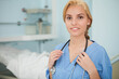 © wavebreak3 - Female clinician in blue scrubs standing right in clinic by bed holding stethoscope, copy space
