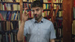 © Krakenimages.com - Hispanic man smiles while performing ok sign with hand in library building; approval confidence trust positivity.