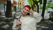© Krakenimages.com - Woman smiling in city street holding tennis racket making peace gesture wearing white sweater and red headband outdoors surrounded by urban landscape.
