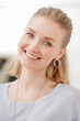 © Miramiska - A beautiful blonde woman smiles warmly, wearing a casual gray top and large hoop earrings.  A joyful and inviting portrait.