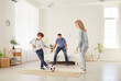 © Studio Romantic - Active sporty happy funny family, excited little boy playing football with father, mother at home, young parents and small child son having fun spending time together in new spacious living room
